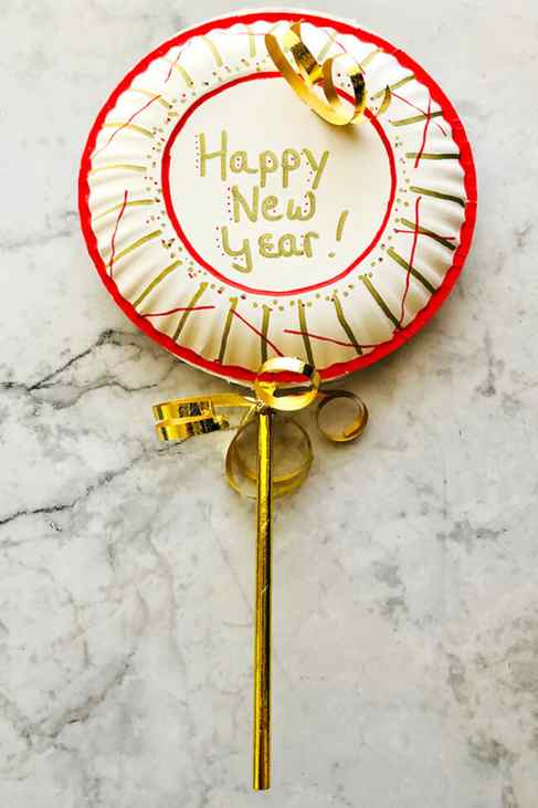 noisemaker made with paper plate with golden ribbon and red details on a marbled background