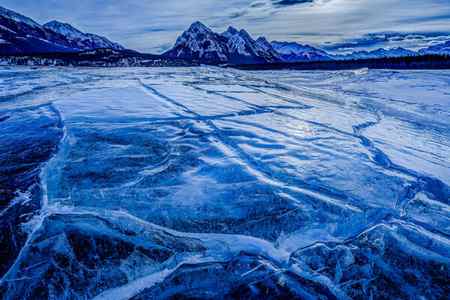 a winter scene of cracks in the ice in Abraham Lake with mountains in the backgroud