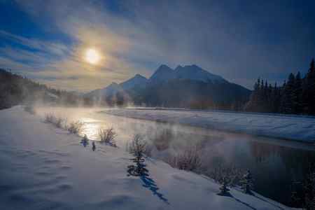 A setting sun reflecting in a river in a winter scene in the mountains in the Canadian Rockies