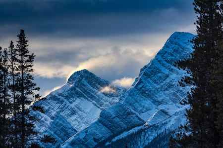 a winter scene of snow blowing off the tops of mountains at sunrise in Canada