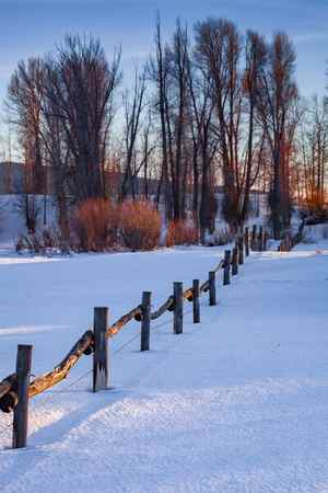 A winter scene of snow-covered ground and a fence in Grand Teton National Park