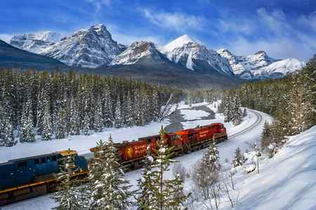A red train passing in front of the snow-covered mountains in the winter at Morant