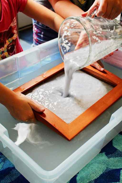 Pouring blended paper and water into a mould and deckle in a tub of water.