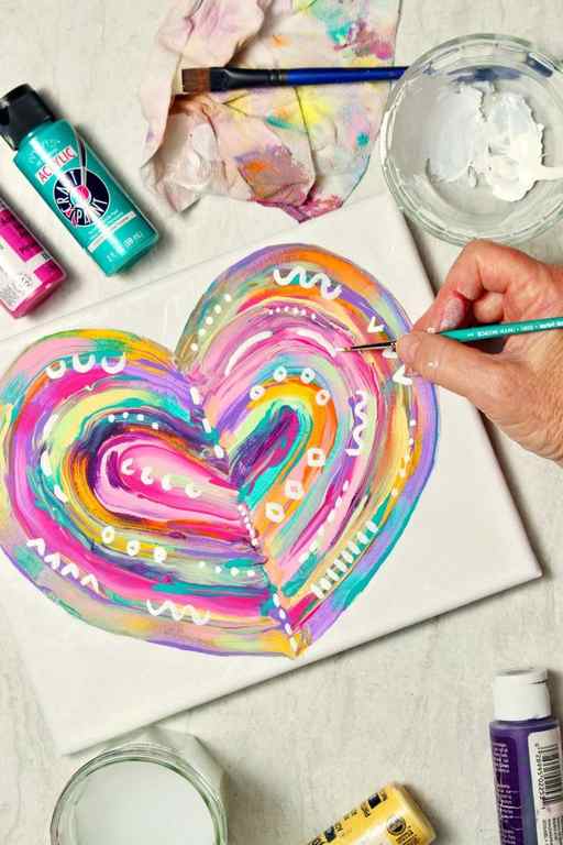 Hand painting finishing touches on completed abstract heart painting with paint supplies near by.