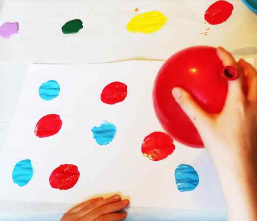 Image shows a hand holding a red balloon to make a painting. Idea from Teaching Ideas