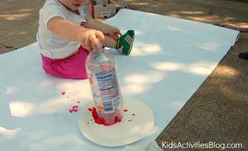 Step 4 - Paint Flowers with Water Bottles - Add paint to a paper plate, and dip a water bottle into it- little girl stamping paint and water bottle on a large sheet of paper to make flowers