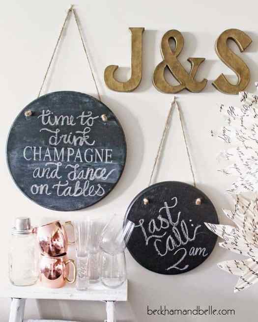 Round hanging chalkboard art above white side table with assorted glasses and bronze letter art. 