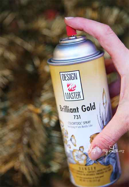A can of floral design master brilliant gold spray paint held in front of a DIY gold Christmas tree. -Skip To My Lou