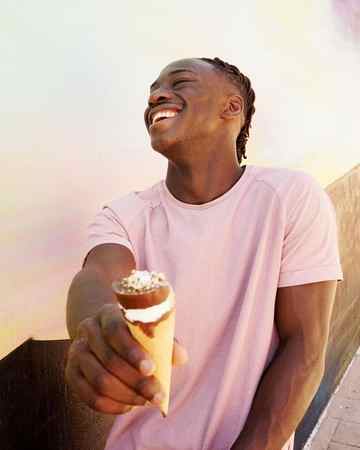 Smiling Teenage Boy Holding Ice Cream Cone While Standing Against Building