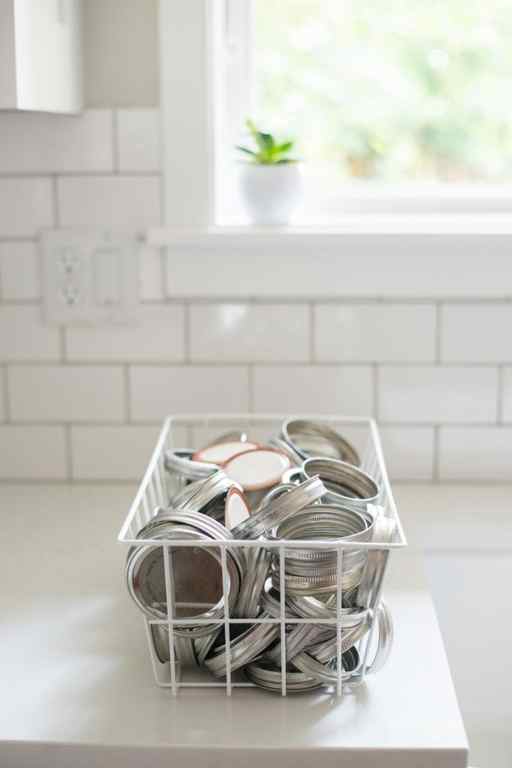 white wire basket filled with metal mason jar lids on white kitchen countertop
