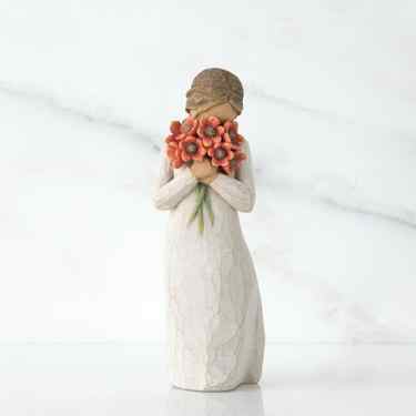 Small girl figurine wearing white dress holding red flower boquet in her hands