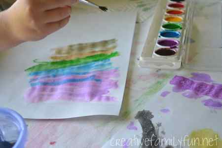 A child painting a rainbow of stripes using watercolours.