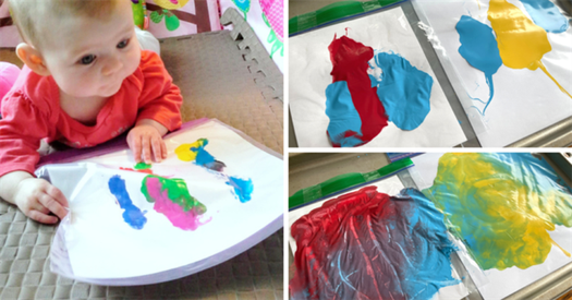 Baby uses hands to move paint inside a clear resealable bag.