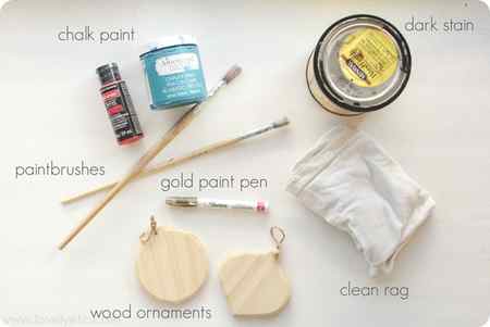 materials for diy christmas ornaments - craft paint, paintbrushes, dark wood stain, gold paint pen, clean rag, and wooden ornament cut outs.