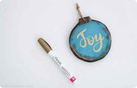 gold paint pen next to DIY wood ornament with the word Joy written in gold ink.