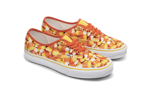 A pair of low top sneakers covered with a candy corn design and orange laces. 