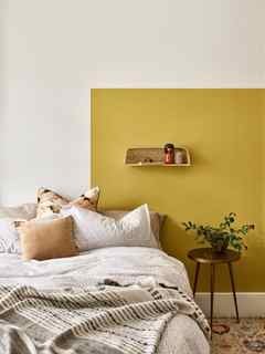 Yellow painted wall behind bed with wicker wall shelf and boho soft furnishings