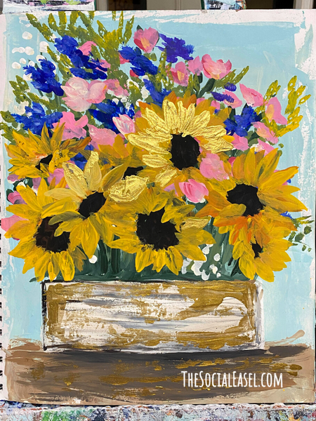  A bouquet of flowers painted on canvas. 8 sunflowers in a box with pink, blue, and white filler flowers. Green foliage. A light blue back ground with a white edge. 