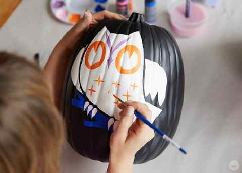 Painting an owl design on a black craft pumpkin