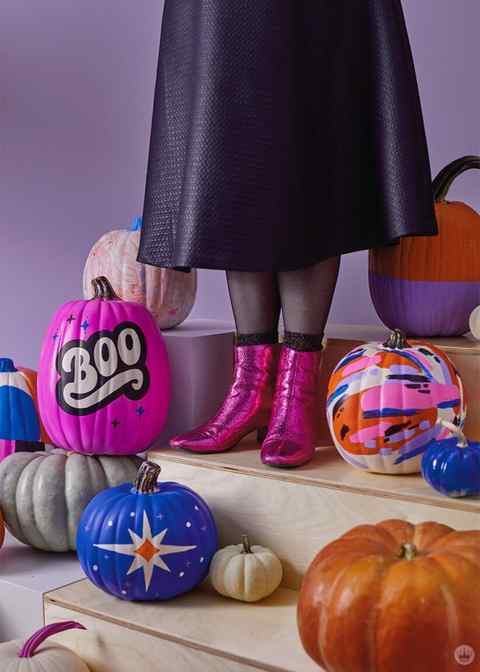 Woman in black skirt and pink metallic boots surrounded by painted pumpkins