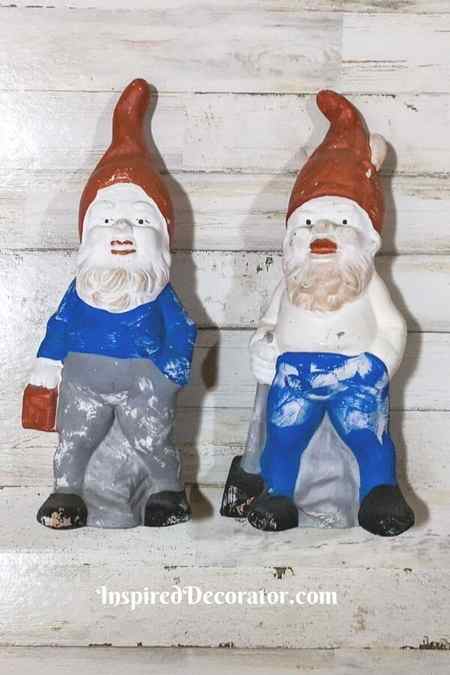 These 2 antique garden gnomes are sun-faded and chipped from age. They are need of a cleaning and restoration. One gnome is holding a lantern, and the other gnome has a sledgehammer.