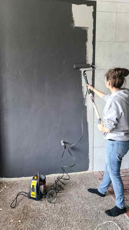 Woman holding electric roller painting the entire wall with gray paint