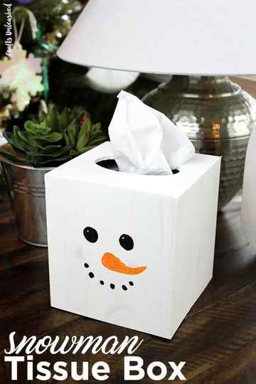 white tissue box with a snowman face painted on it, including a long orange nose, round black eyes and black dots for a smiling mouth it