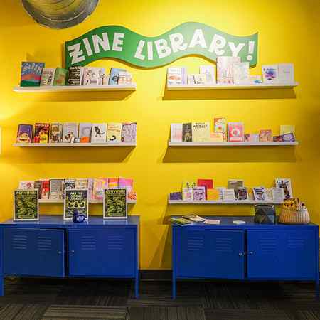 Zine Library against a yellow wall in the E+I center