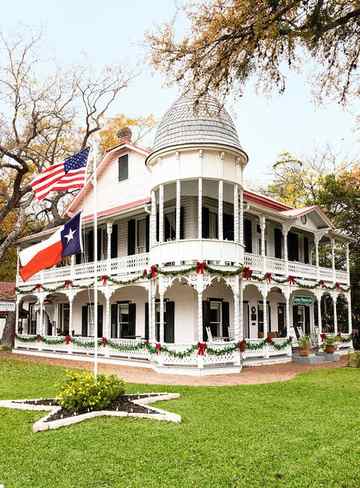 white victorian b and b with two wraparound porches adorned with christmas garland